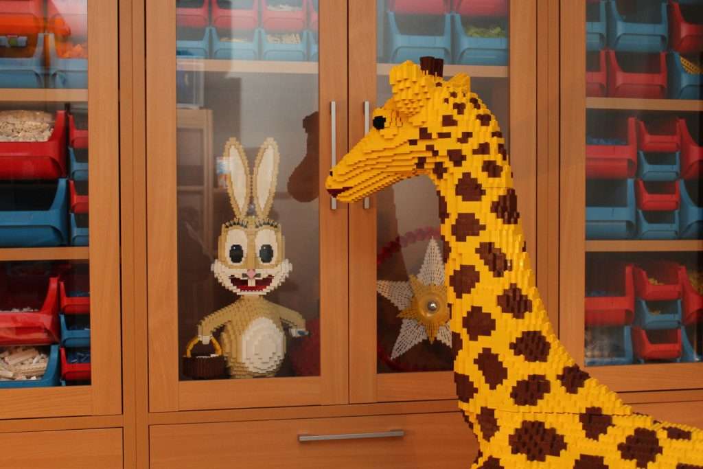 Hasenskulptur und sortierte Legoschachteln in einer Schrankwand, vor der die Giraffenskulptur steht